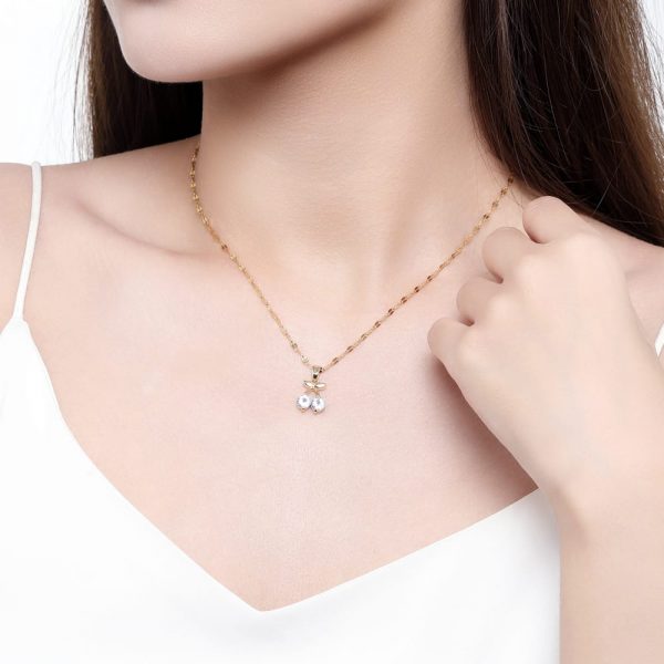 Gold cherry necklace worn on model in white top, close-up on neckline